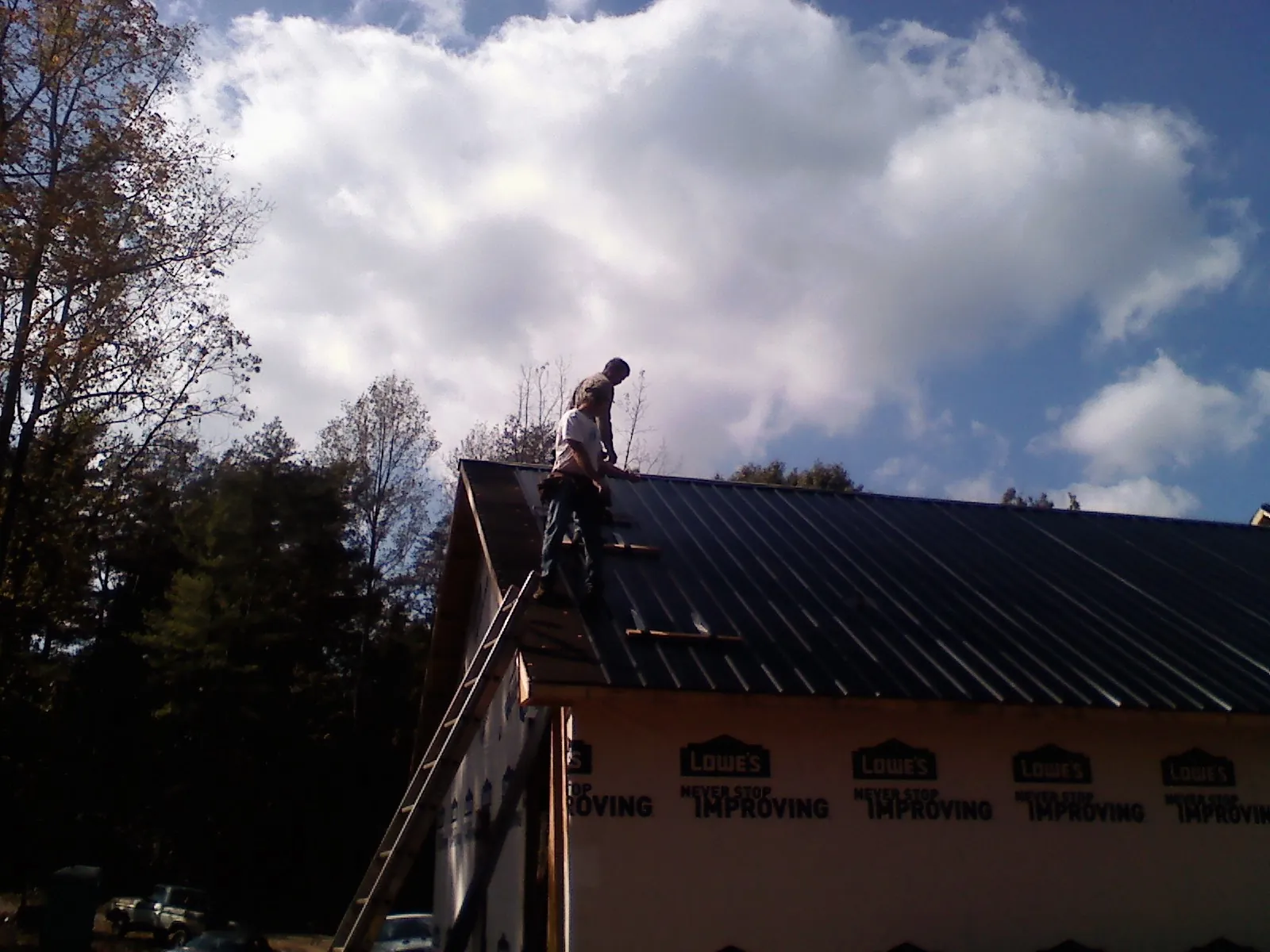 Roofer fastening dark metal panels high against a cloudy sky, from a Roof Inspection job in Unionville